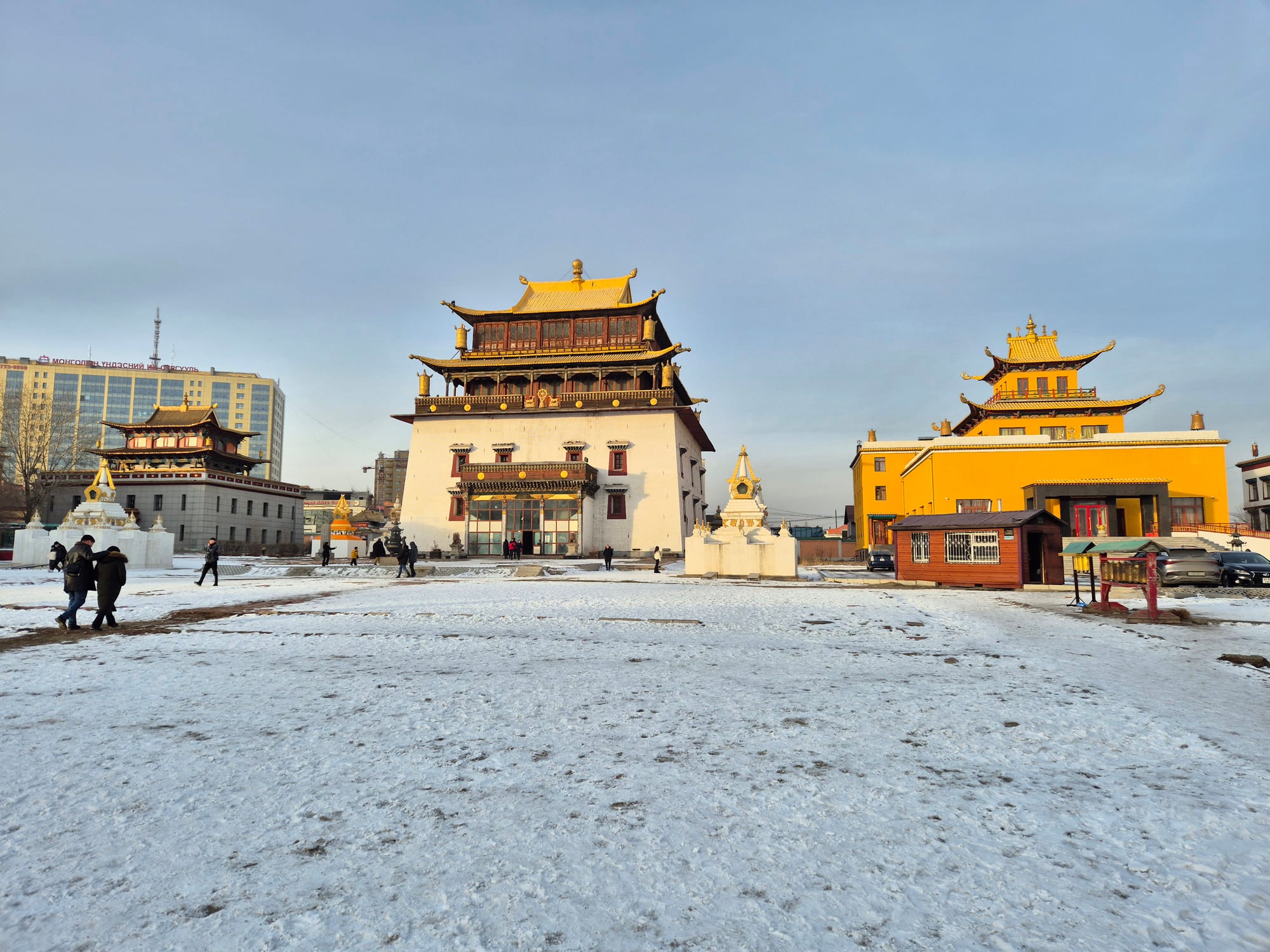 A large Buddhist temple building with a golden roof and prayer wheels along the entrance
