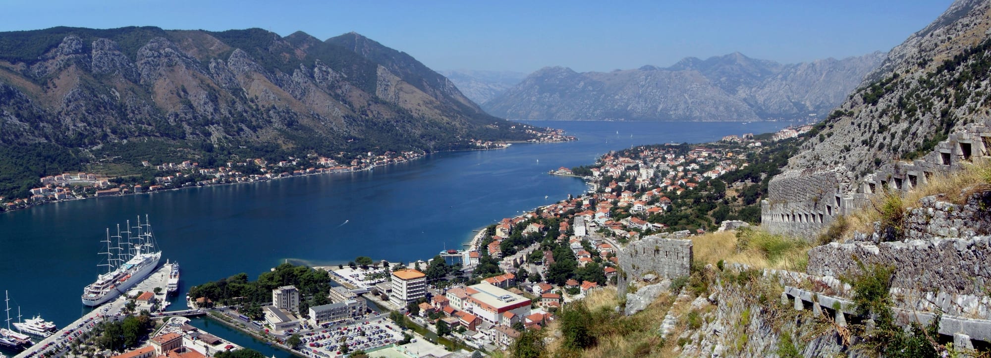 A walled old town on a bay, ringed by steep mountains rising straight from the water