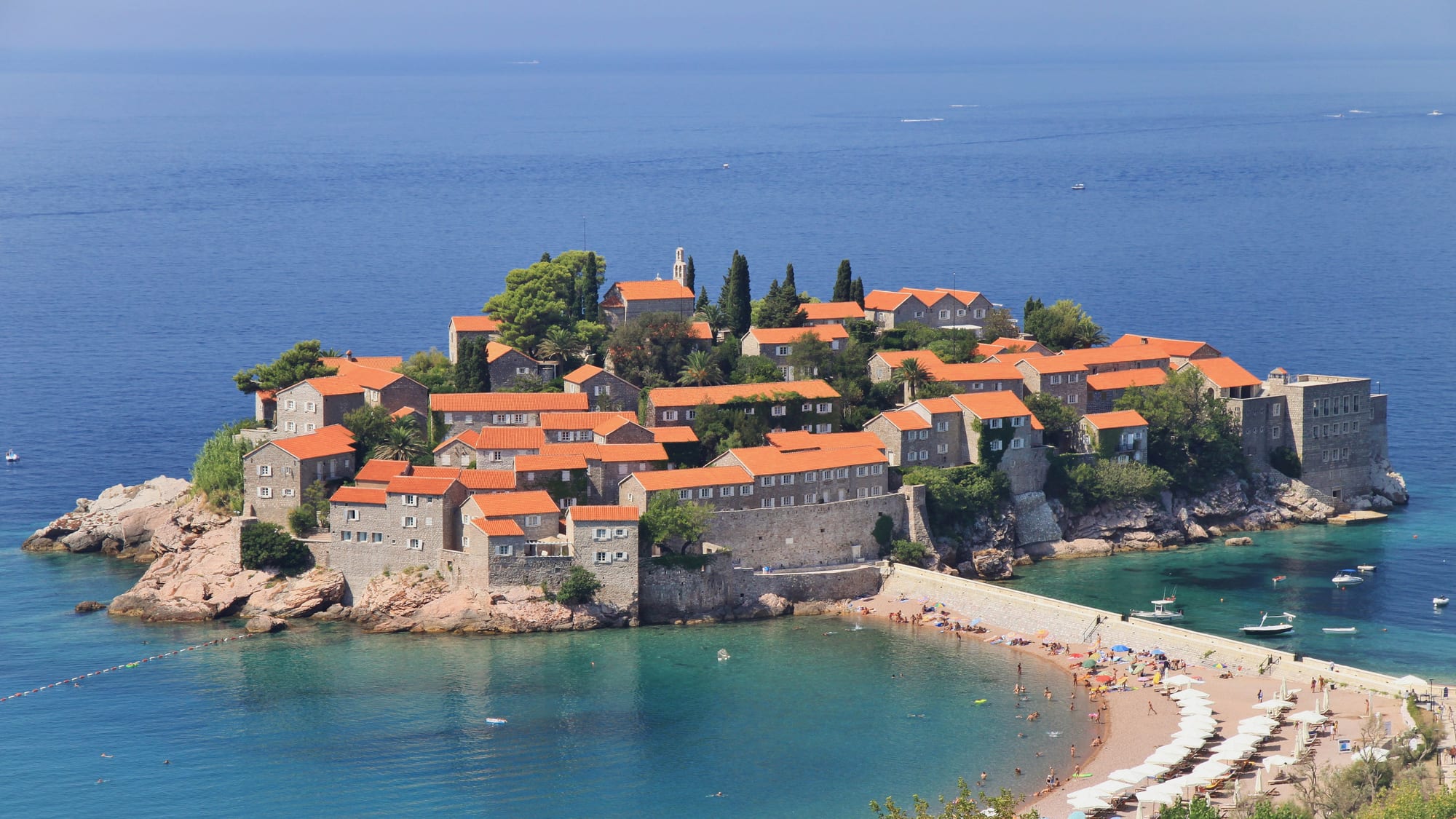 A small island covered in terracotta-roofed stone houses, connected to the shore by a narrow causeway