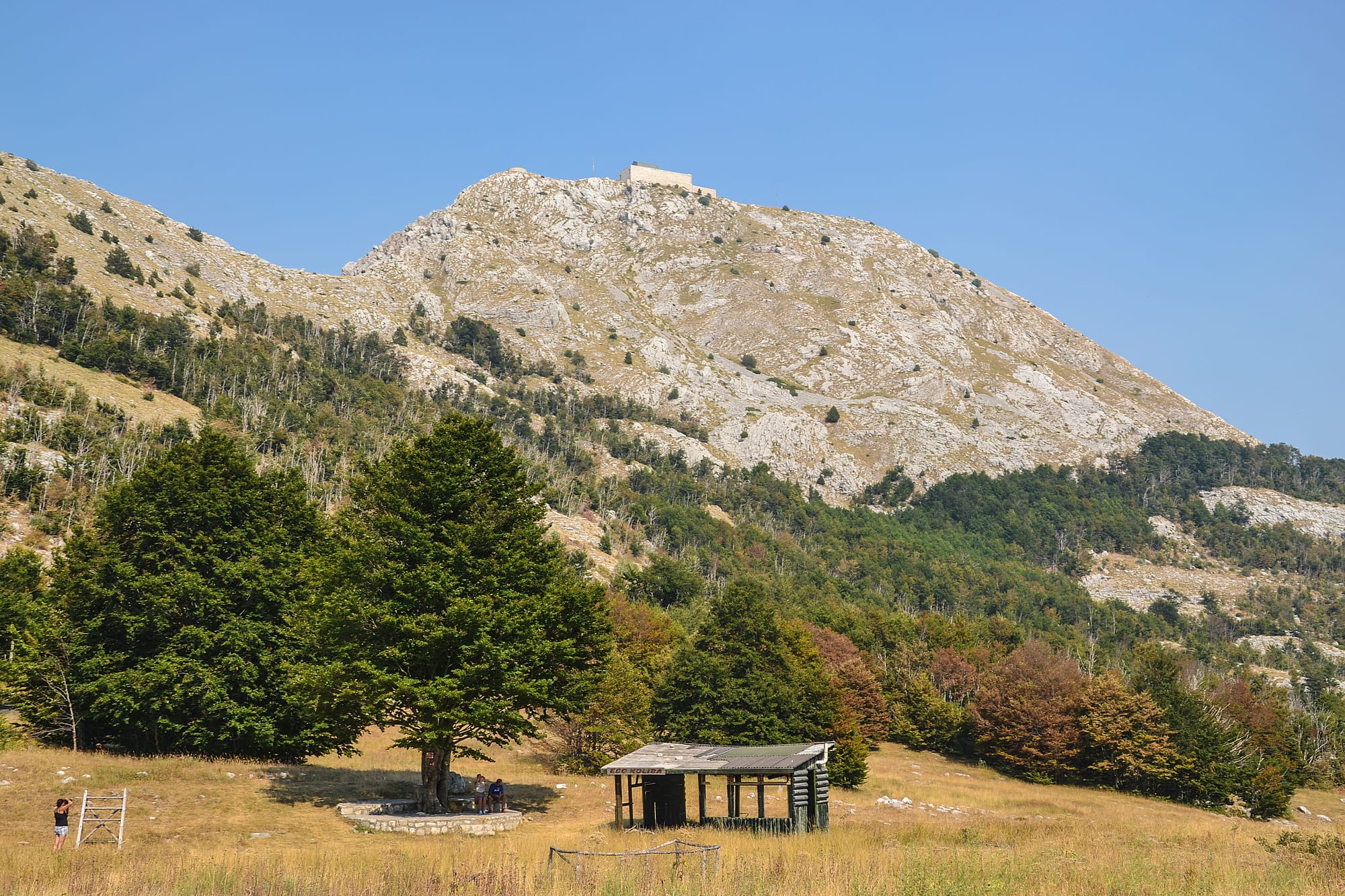 A rugged mountain summit with a mausoleum structure on top, views over a rocky landscape