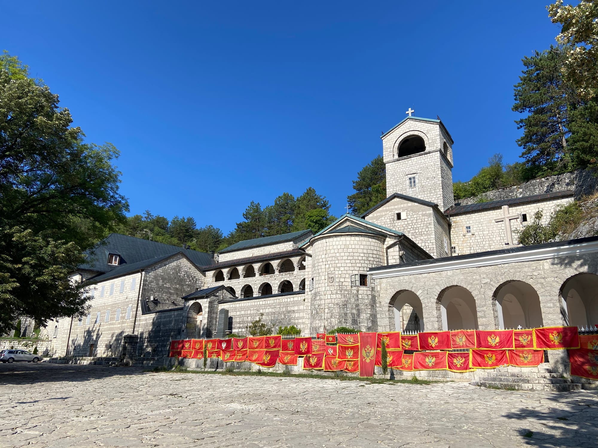 A whitewashed Orthodox monastery with a bell tower, tucked against a bare grey mountainside at Cetinje