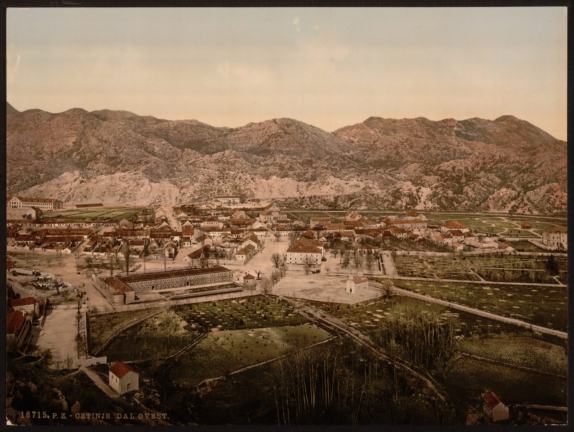 A hand-coloured historic print of a small town of low red-roofed houses on a flat valley floor, walled in by bare grey limestone mountains