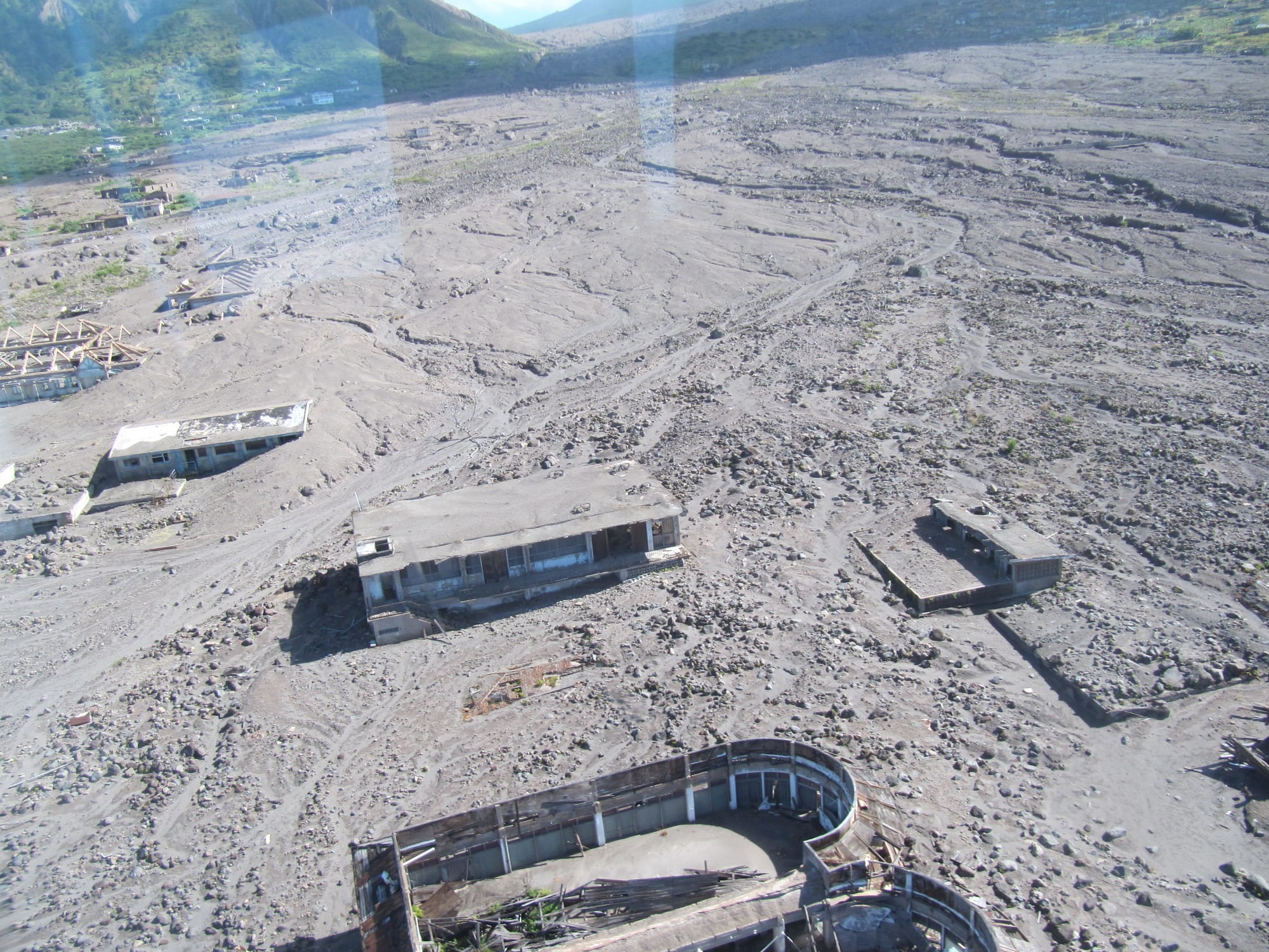 The upper floors of ash-buried buildings protruding from a grey, ash-covered townscape