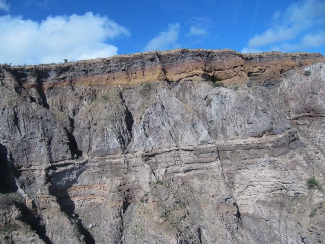 Grey volcanic ash and pyroclastic deposits layered across a devastated hillside landscape