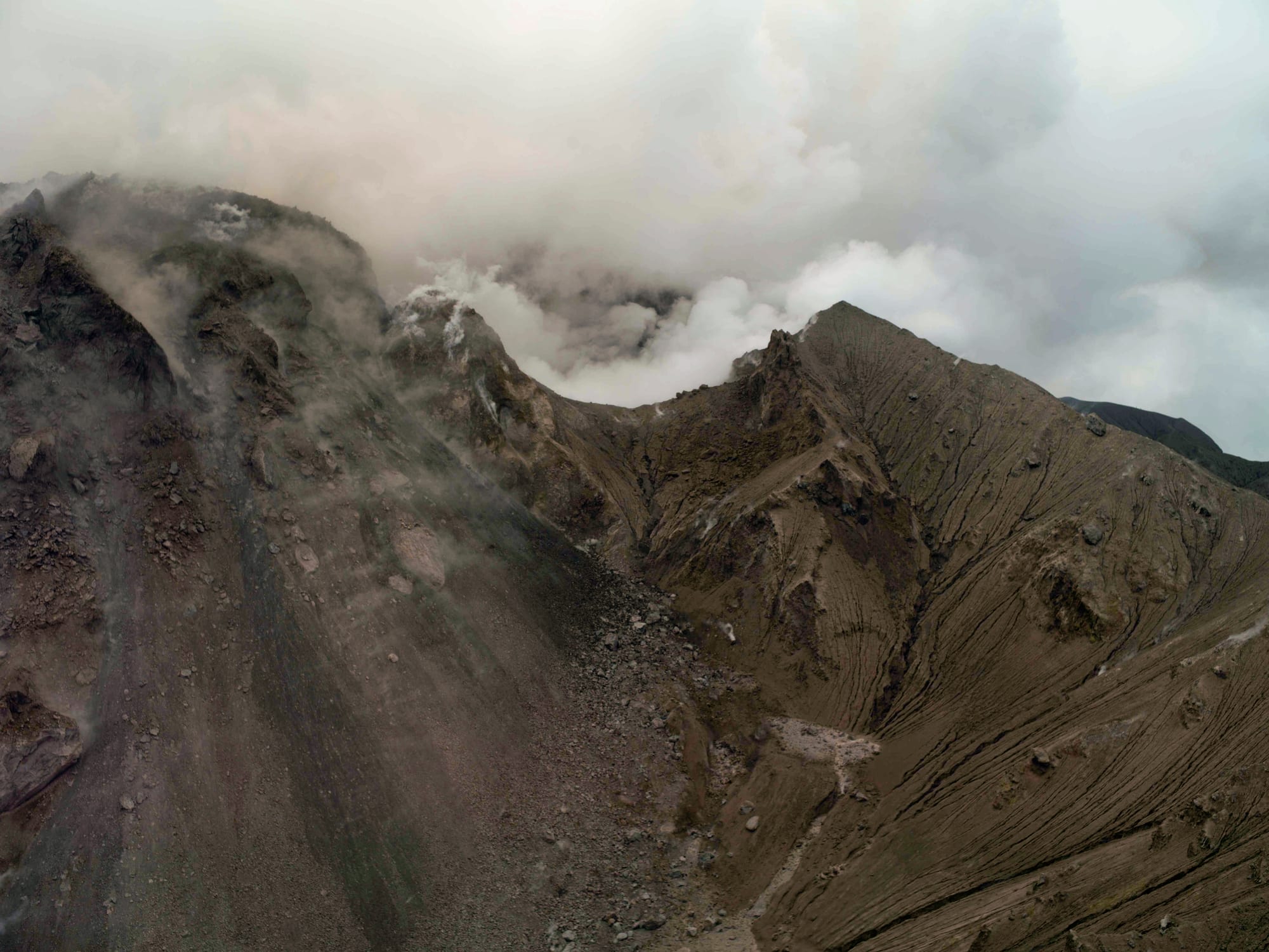 An active volcano with a dome of grey rock and a plume of steam rising above a devastated landscape