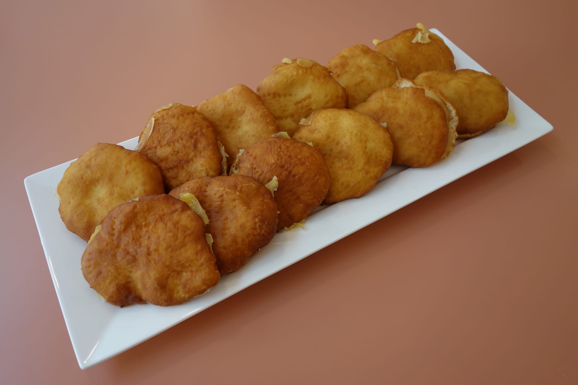 A long white platter piled with round, golden-brown fried johnnycakes