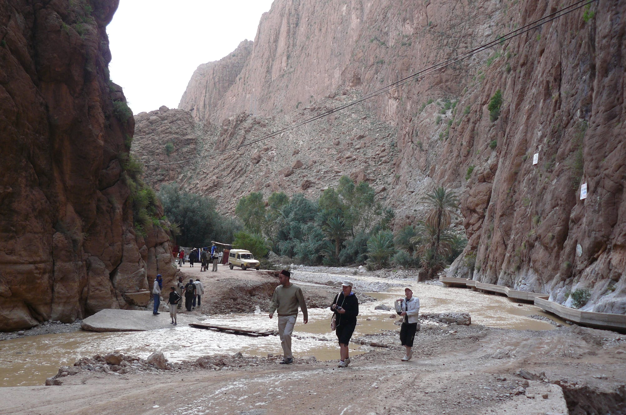 A narrow, towering red rock canyon with a thin road running through the bottom