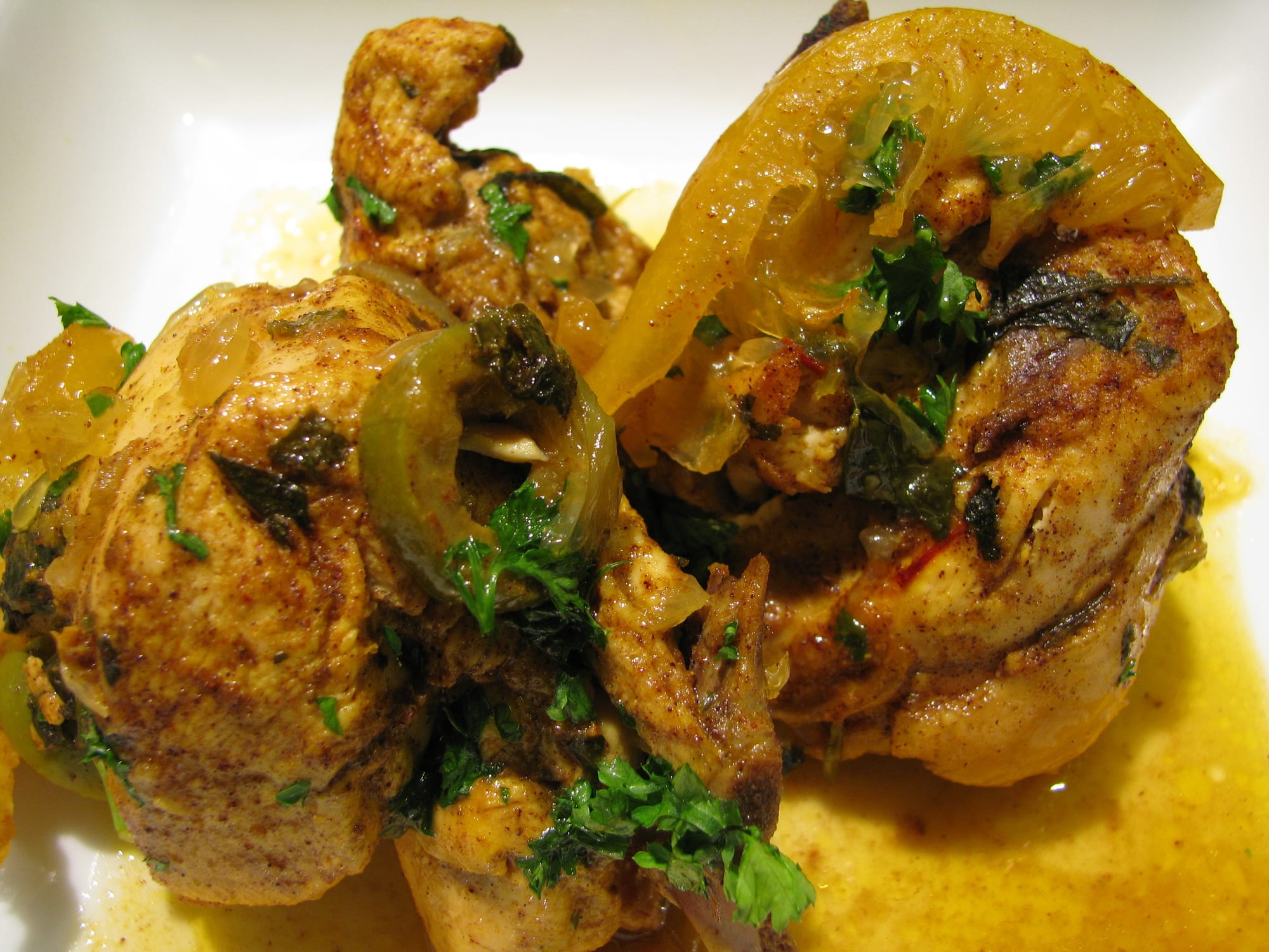 A close-up of chicken pieces in a yellow sauce with strips of softened preserved lemon rind and chopped herbs