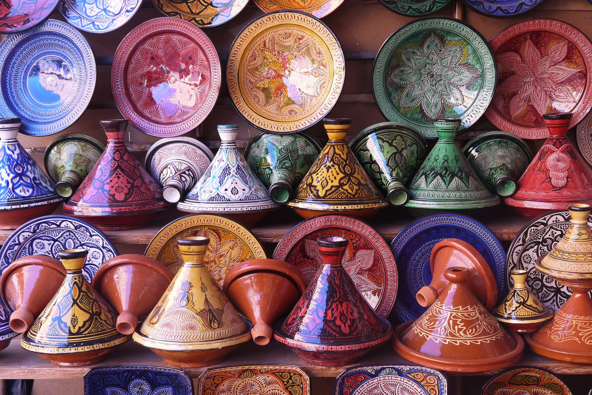 Rows of brightly painted conical earthenware pots and decorated plates stacked on shelves in a shop