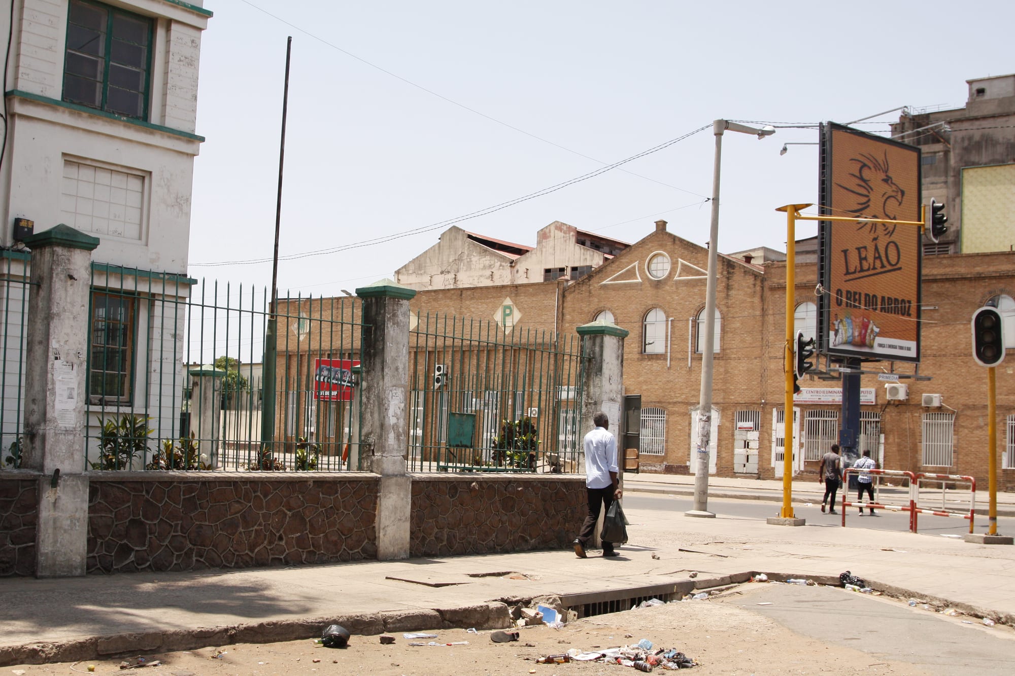 A street in downtown Maputo lined with faded colonial-era buildings, a pedestrian walking past a fenced compound