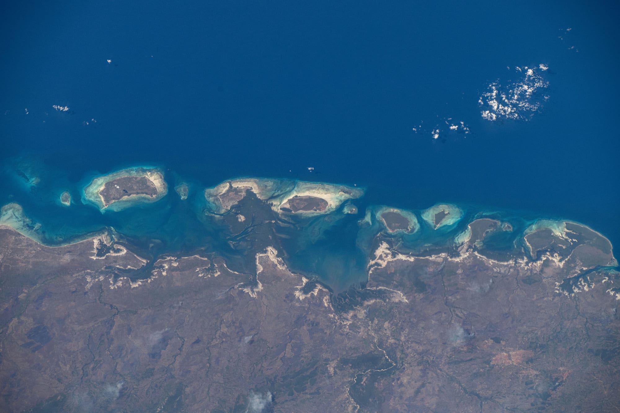 A chain of small green islands and reefs seen from orbit along a coastline