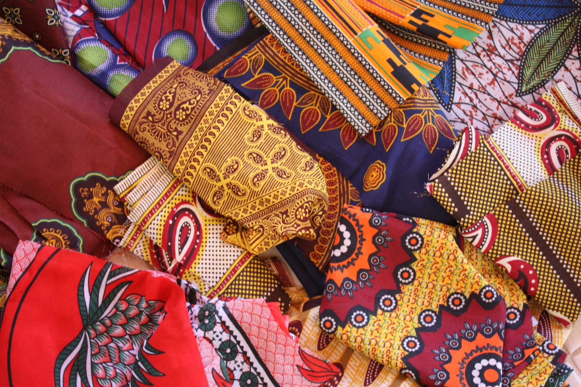 A heap of brightly printed cotton cloths in red, yellow, orange, navy and maroon, with bold floral, paisley and geometric patterns