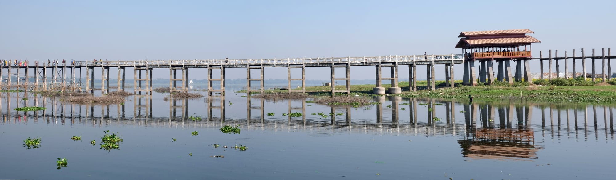 A long wooden footbridge crossing a wide, shallow lake at sunset