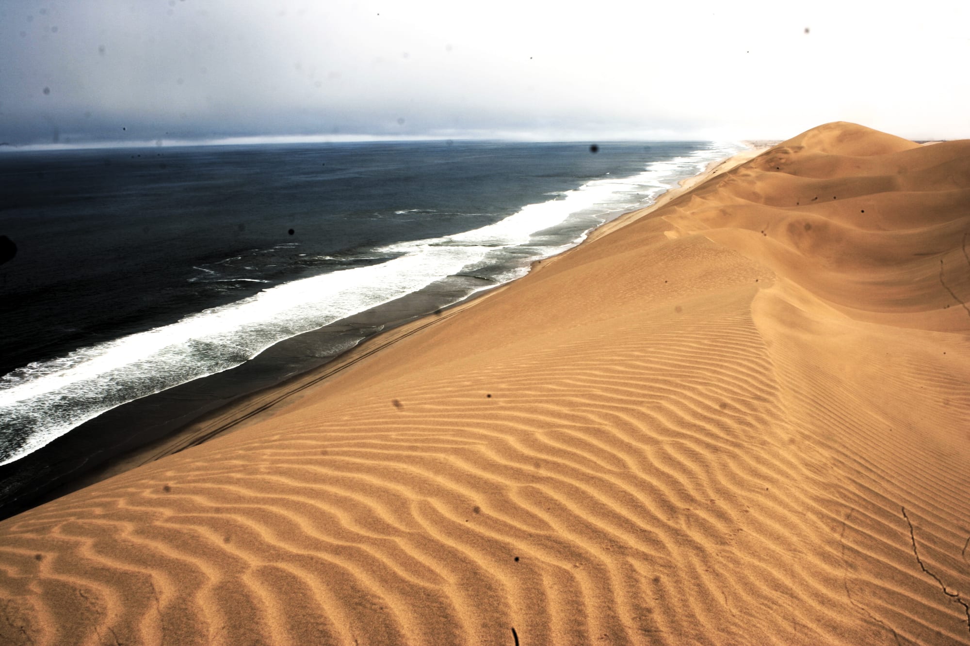 Wind-sculpted sand dunes meeting a foggy, wild Atlantic coastline