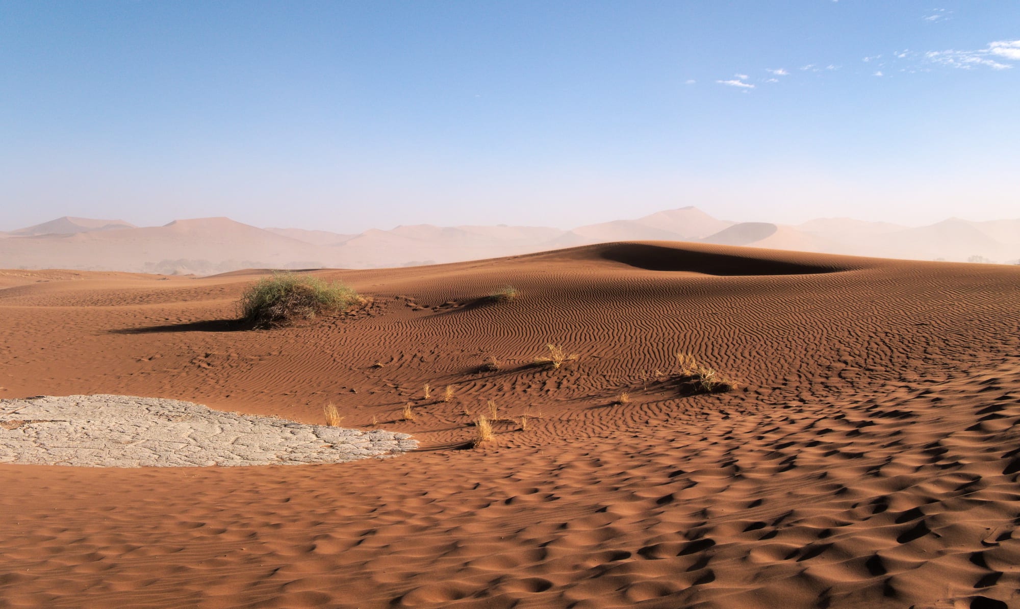 A massive rippled red sand dune with a small figure for scale, under a deep blue sky