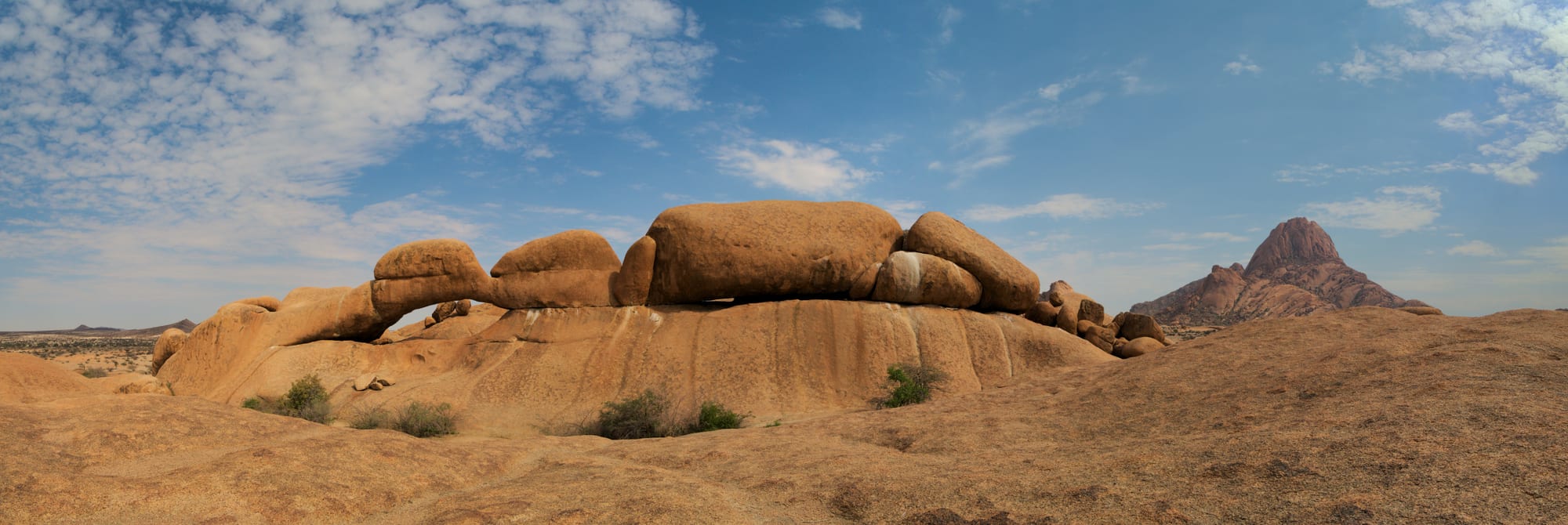 A natural rock arch framing a view of a sharp granite peak in the desert