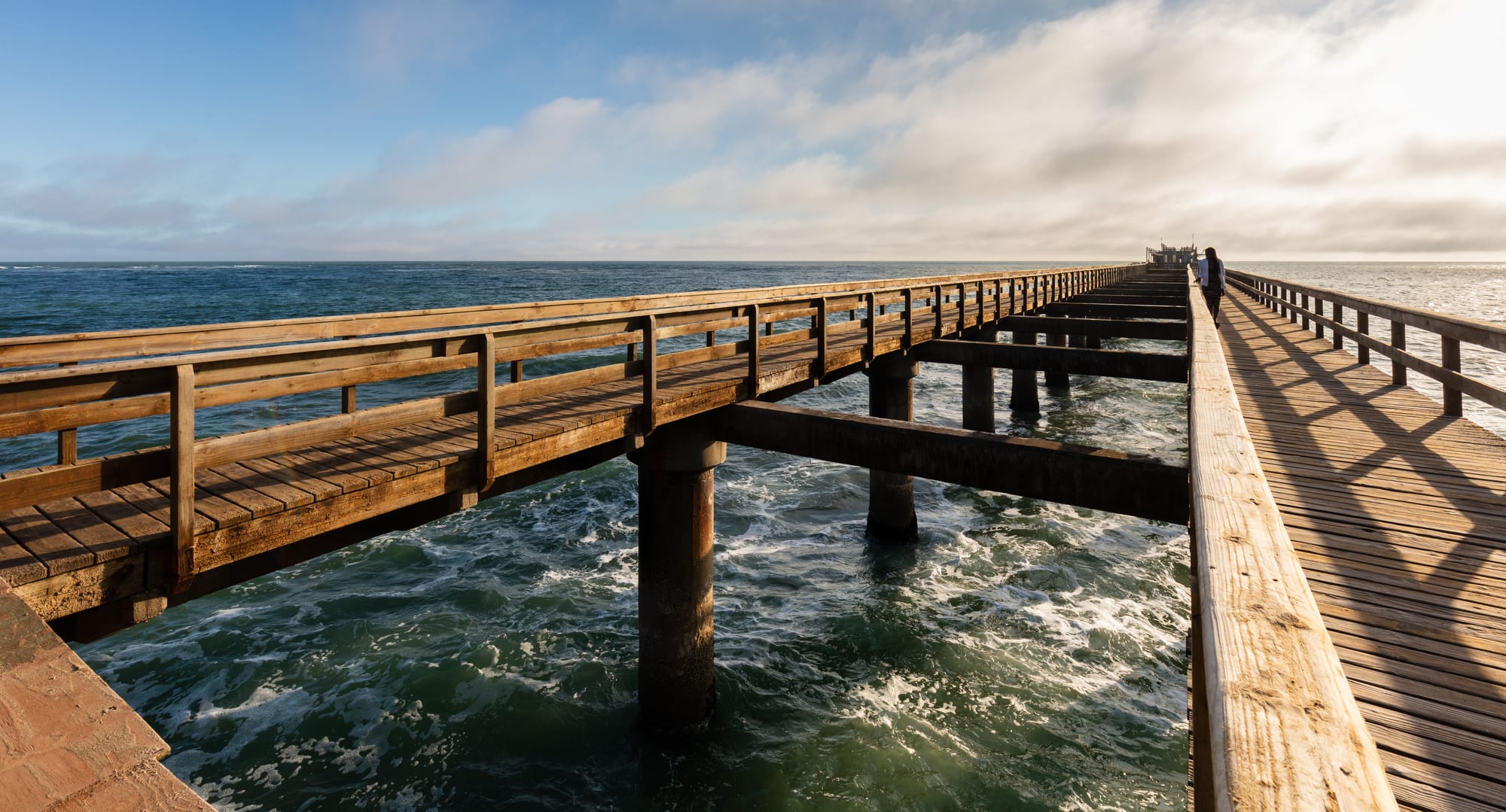 A long wooden pier extending into the sea, with fog along the coast