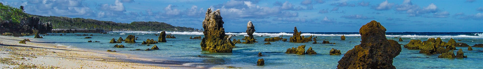 Dark volcanic and coral rocks along a beach with the open ocean beyond