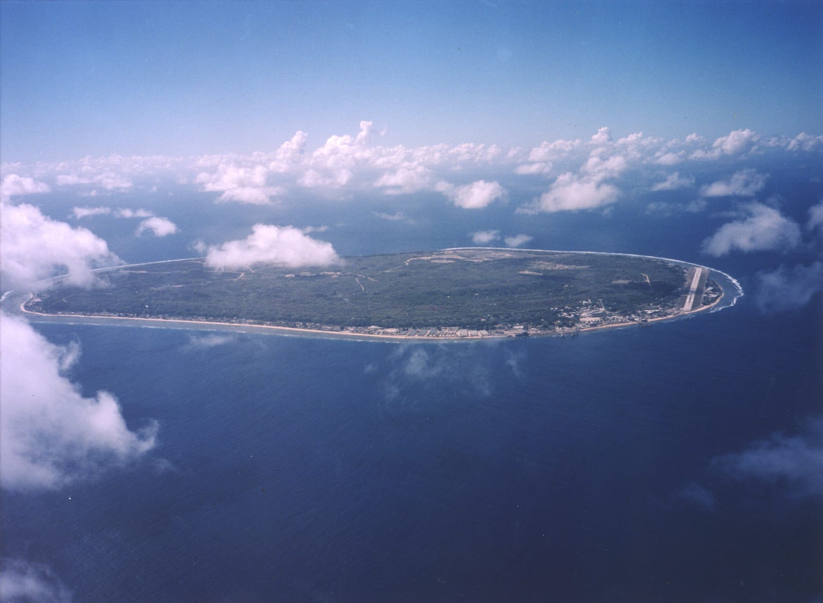 A small round island seen from the air, a green ring of coastal land around a barren pale interior
