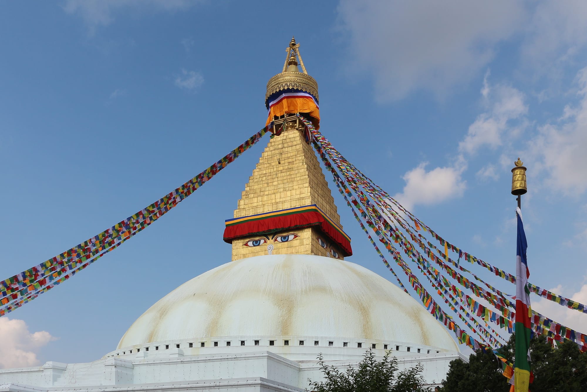 A massive white domed stupa with painted eyes and colourful prayer flags, ringed by buildings