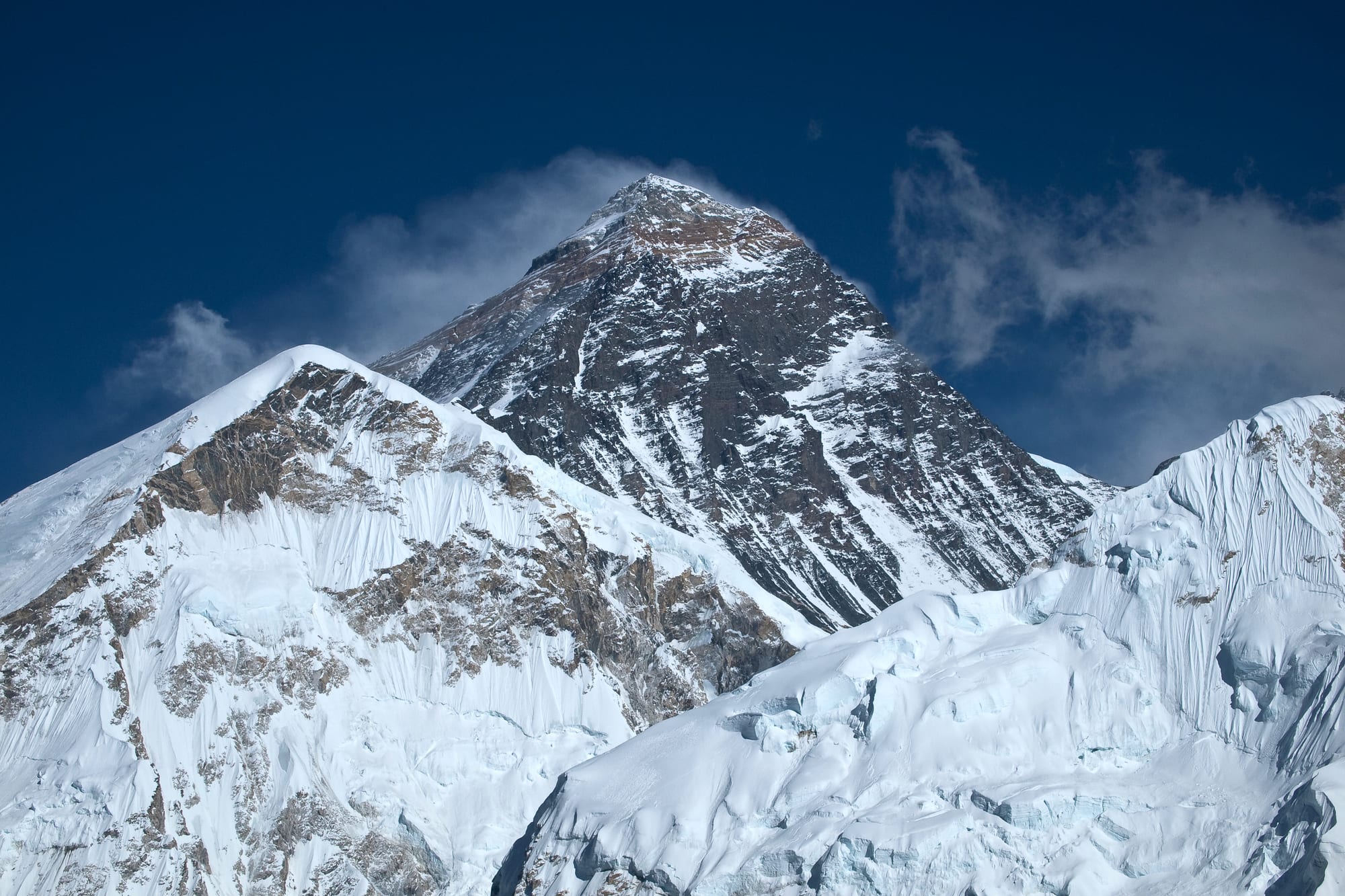 The snow-covered pyramid of Mount Everest rising above a wall of jagged Himalayan peaks