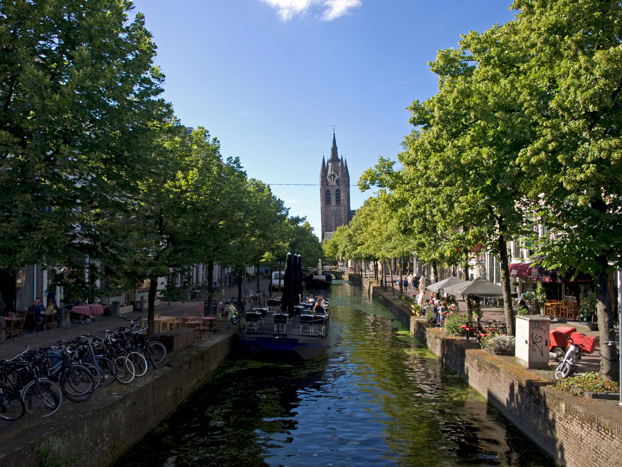 A tree-lined canal with historic gabled houses and a church tower