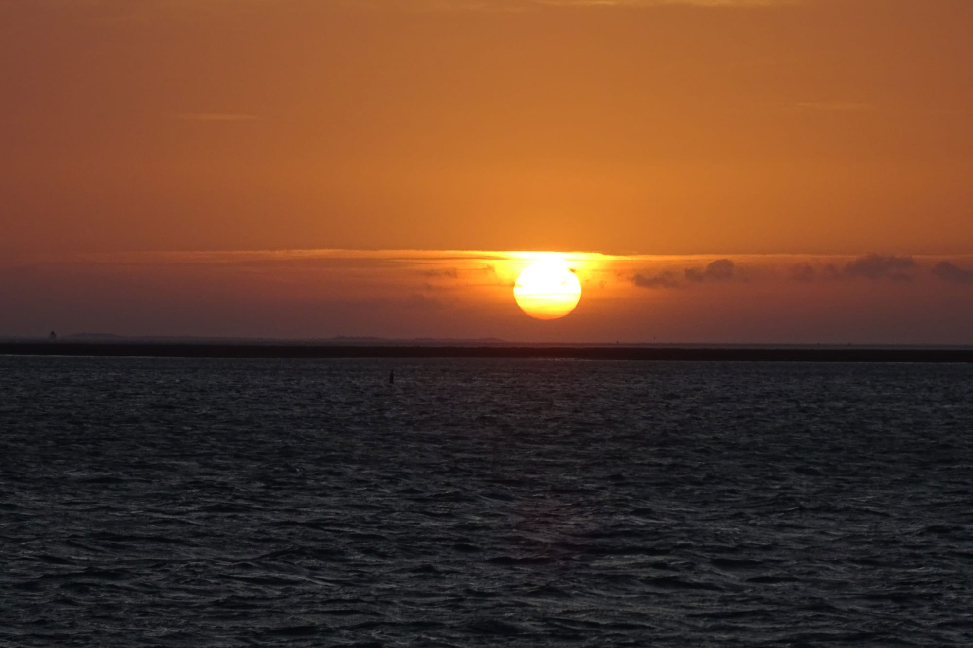 The sun setting over a dark tidal sea with an exposed sandbar on the horizon
