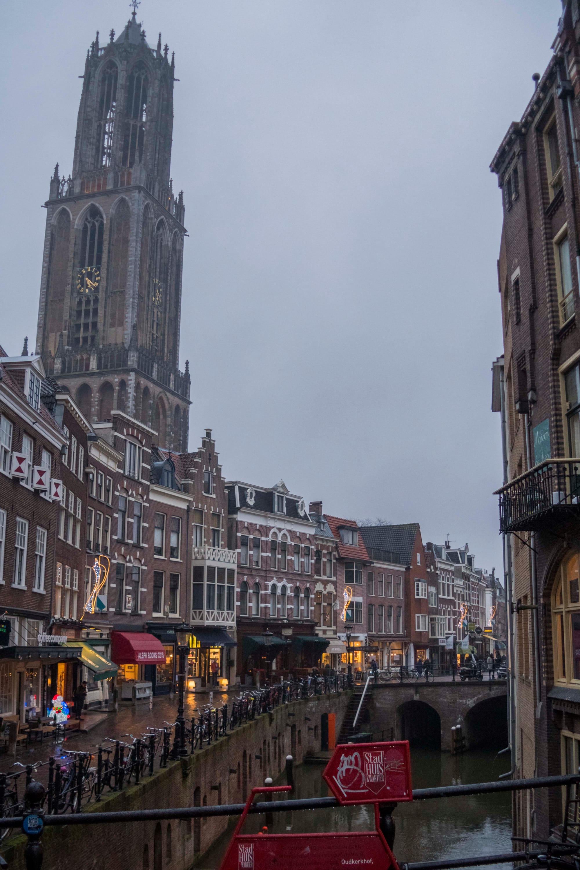 A tall Gothic cathedral tower rising above canal-side townhouses
