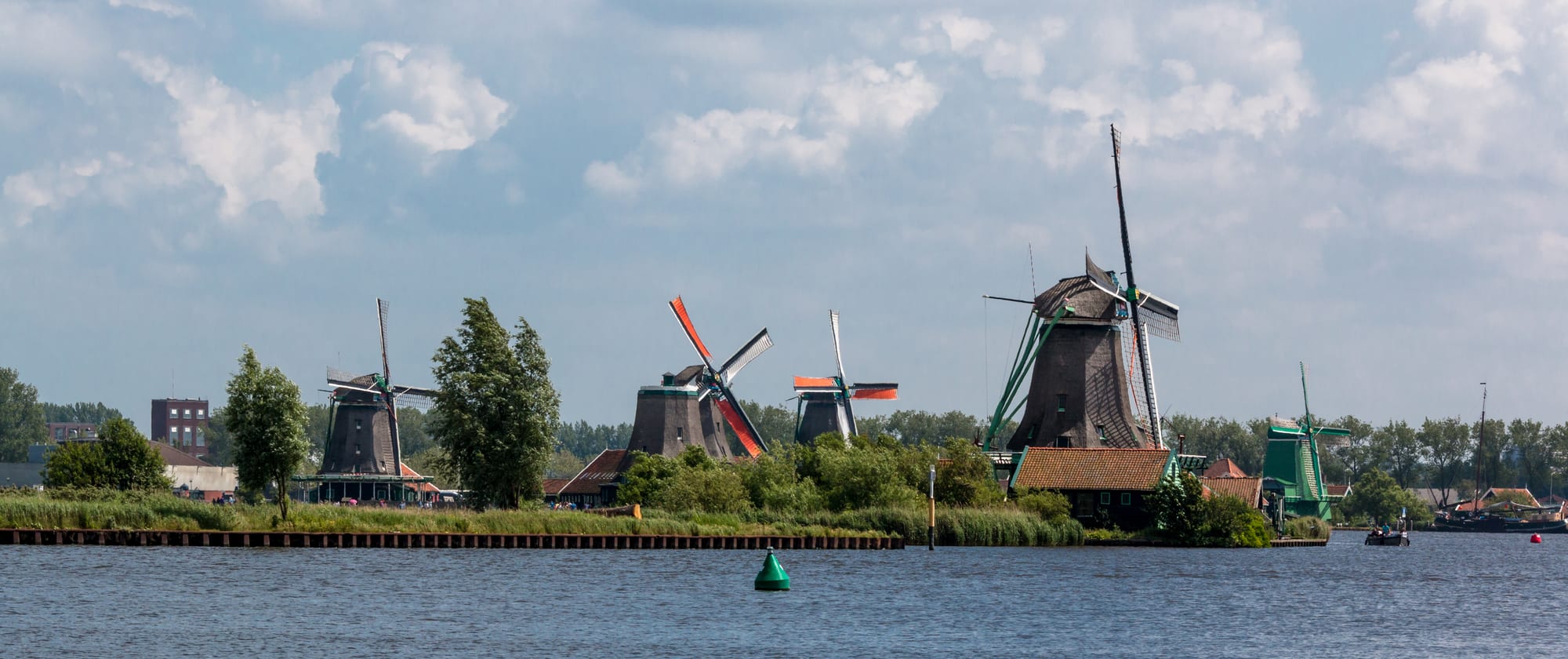 Traditional green wooden windmills and houses along a riverbank