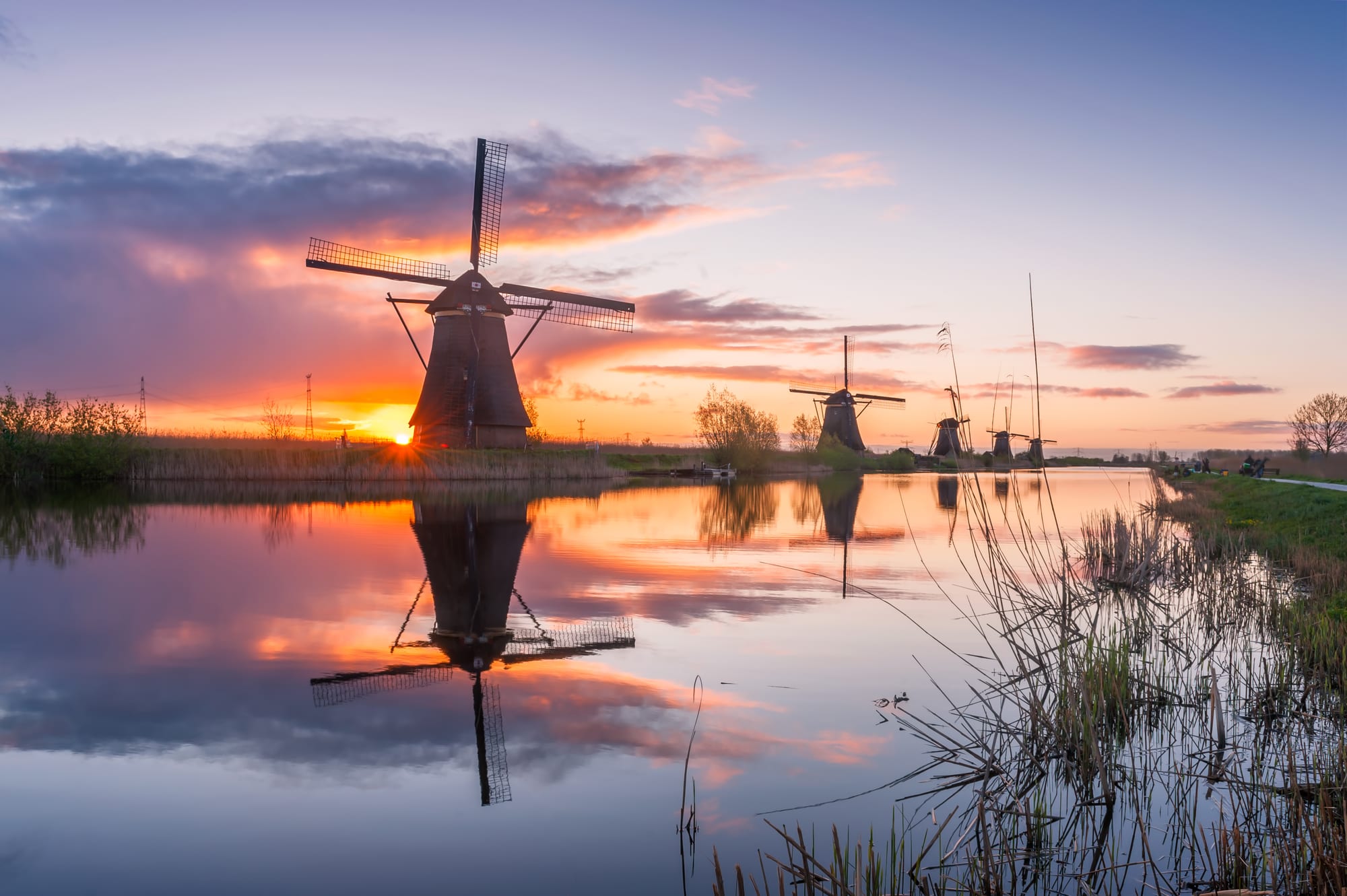 A single windmill silhouetted against a colourful sunrise sky over a canal