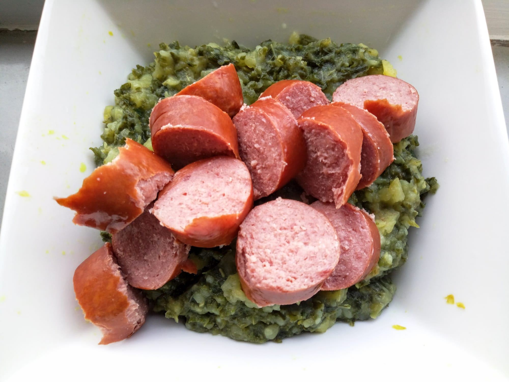 Mashed potato mixed with kale, topped with sliced smoked sausage