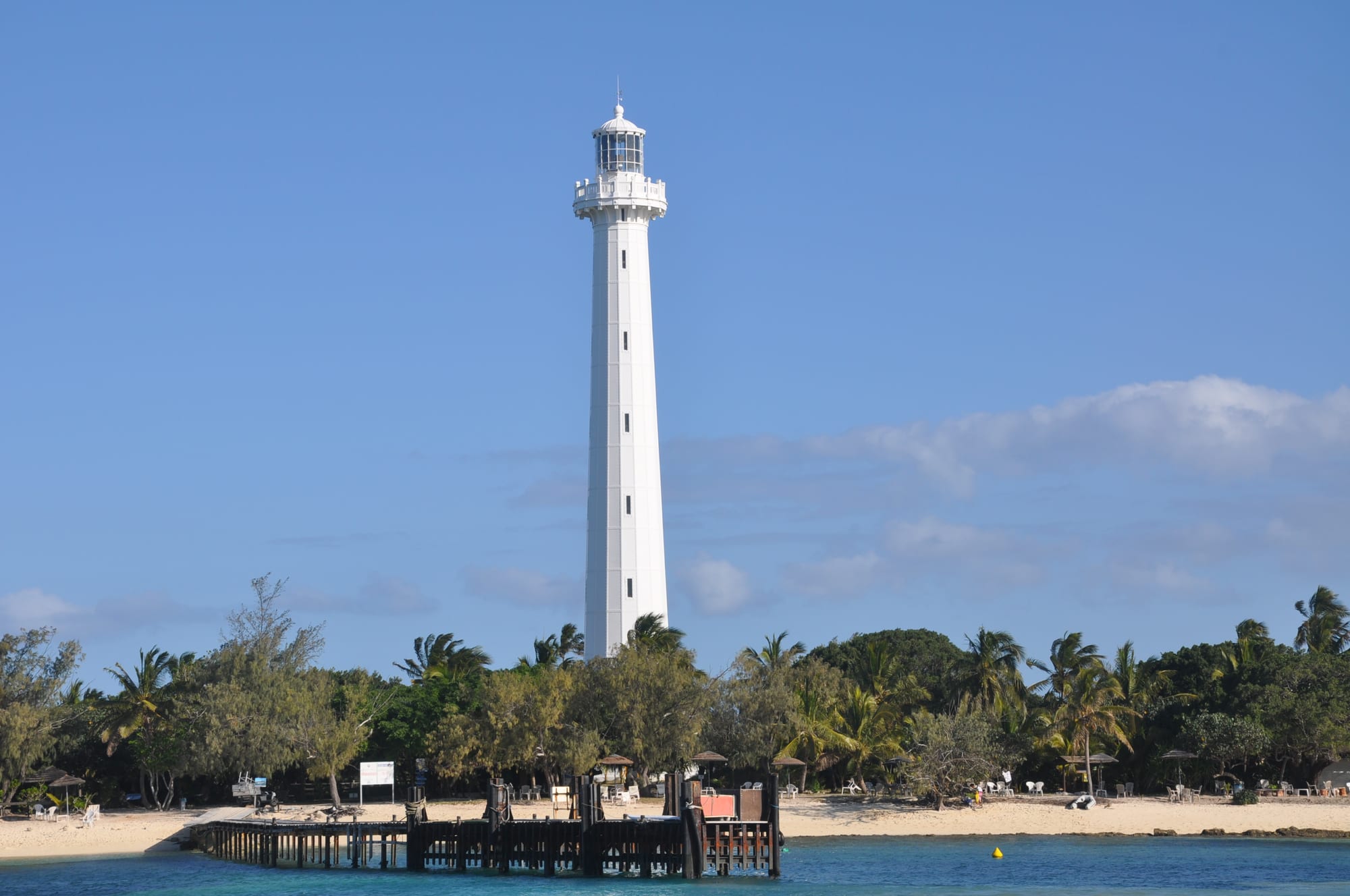 A tall cast-iron lighthouse on a small sandy islet surrounded by turquoise water