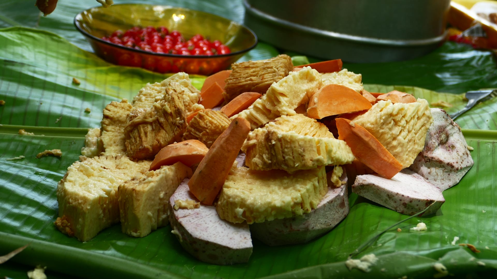 Root vegetables and meat wrapped in banana leaves cooking over a fire