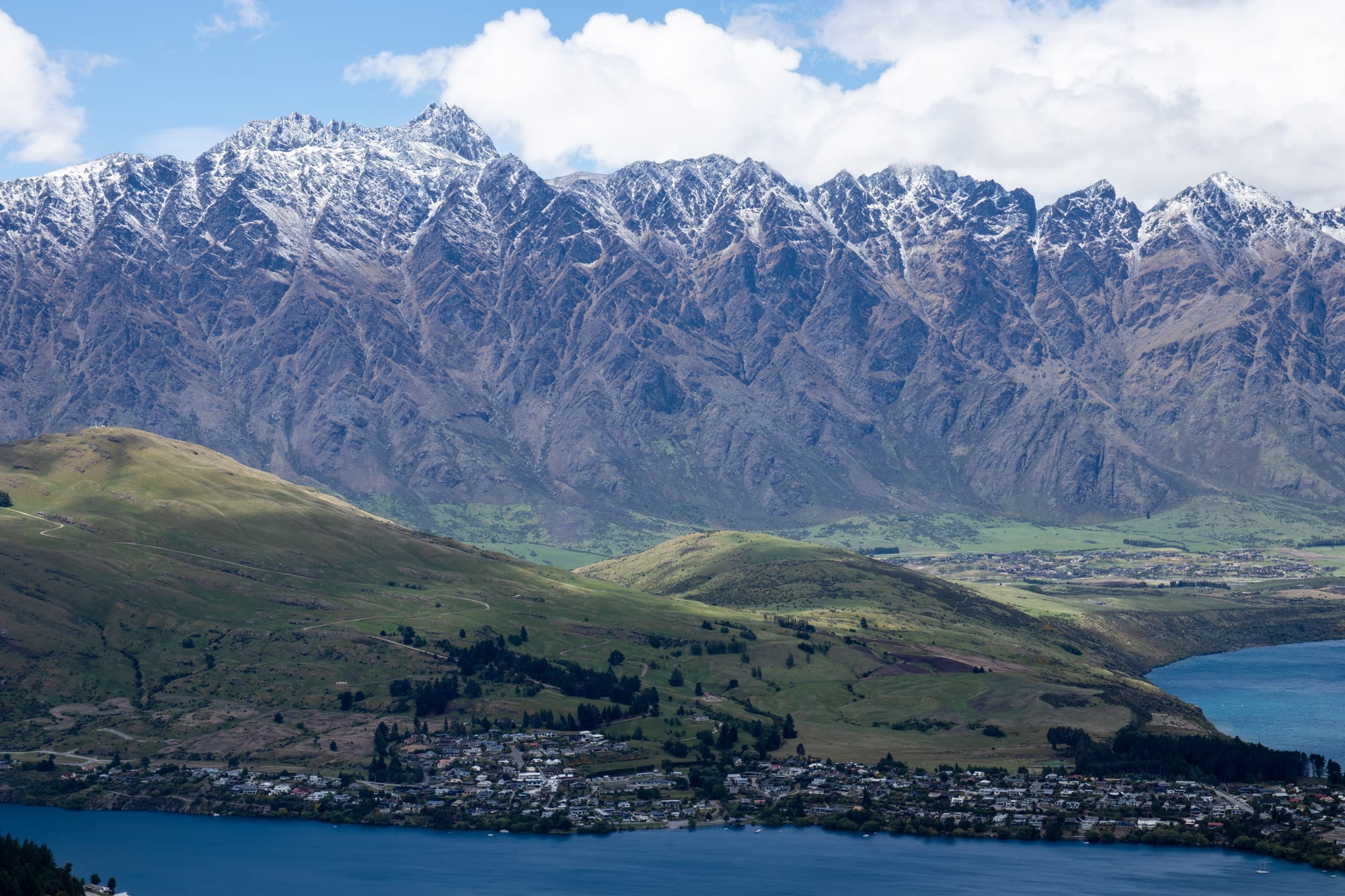 A lakeside town with jagged snow-capped mountains rising directly behind it
