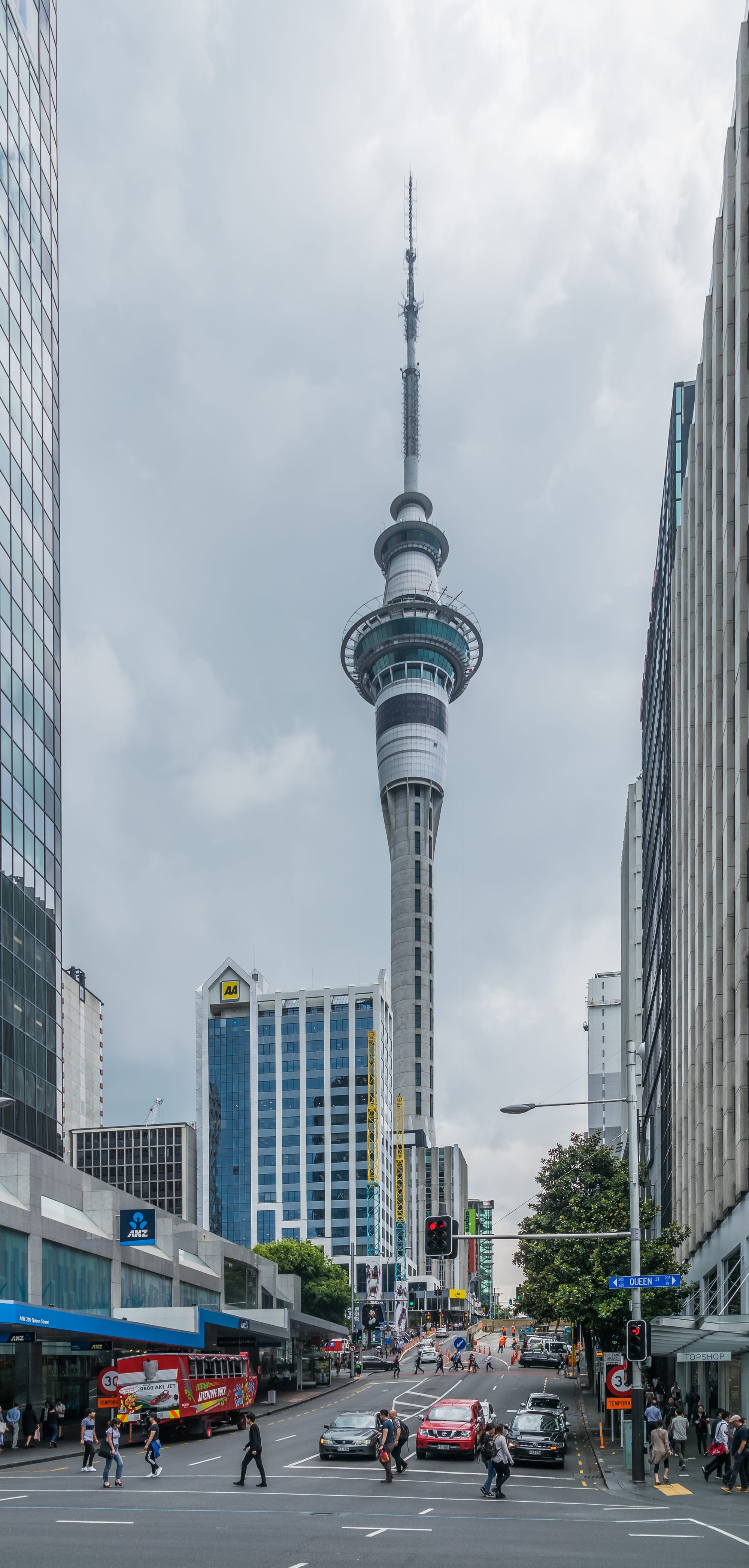 A tall slender observation tower rising above a harbour city skyline