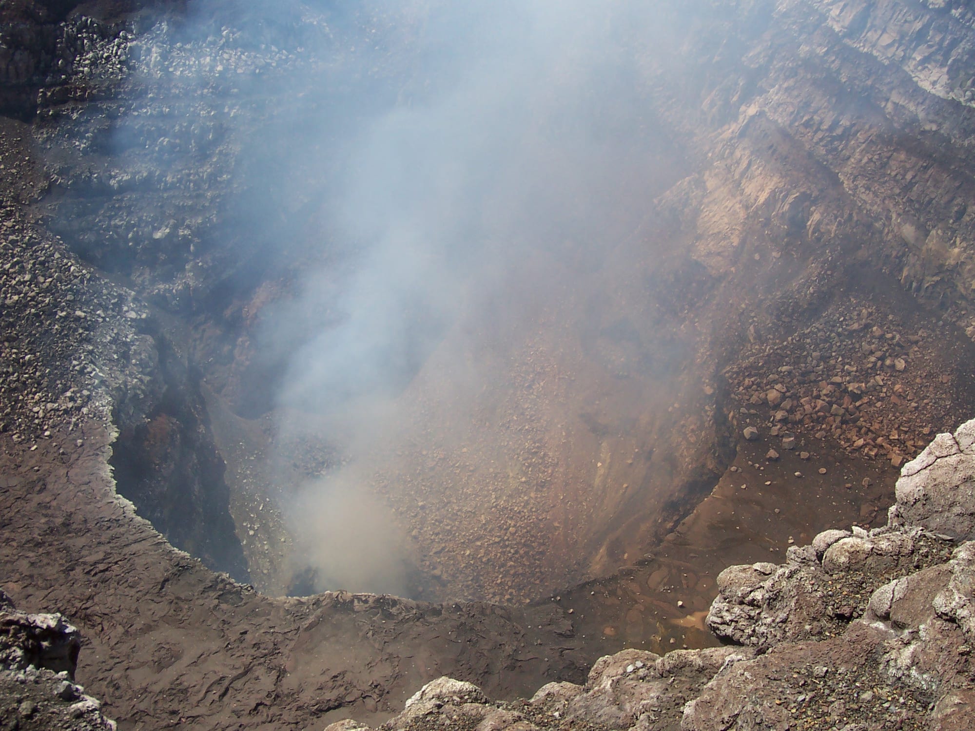A wide volcanic crater with steep grey walls and steam rising from vents