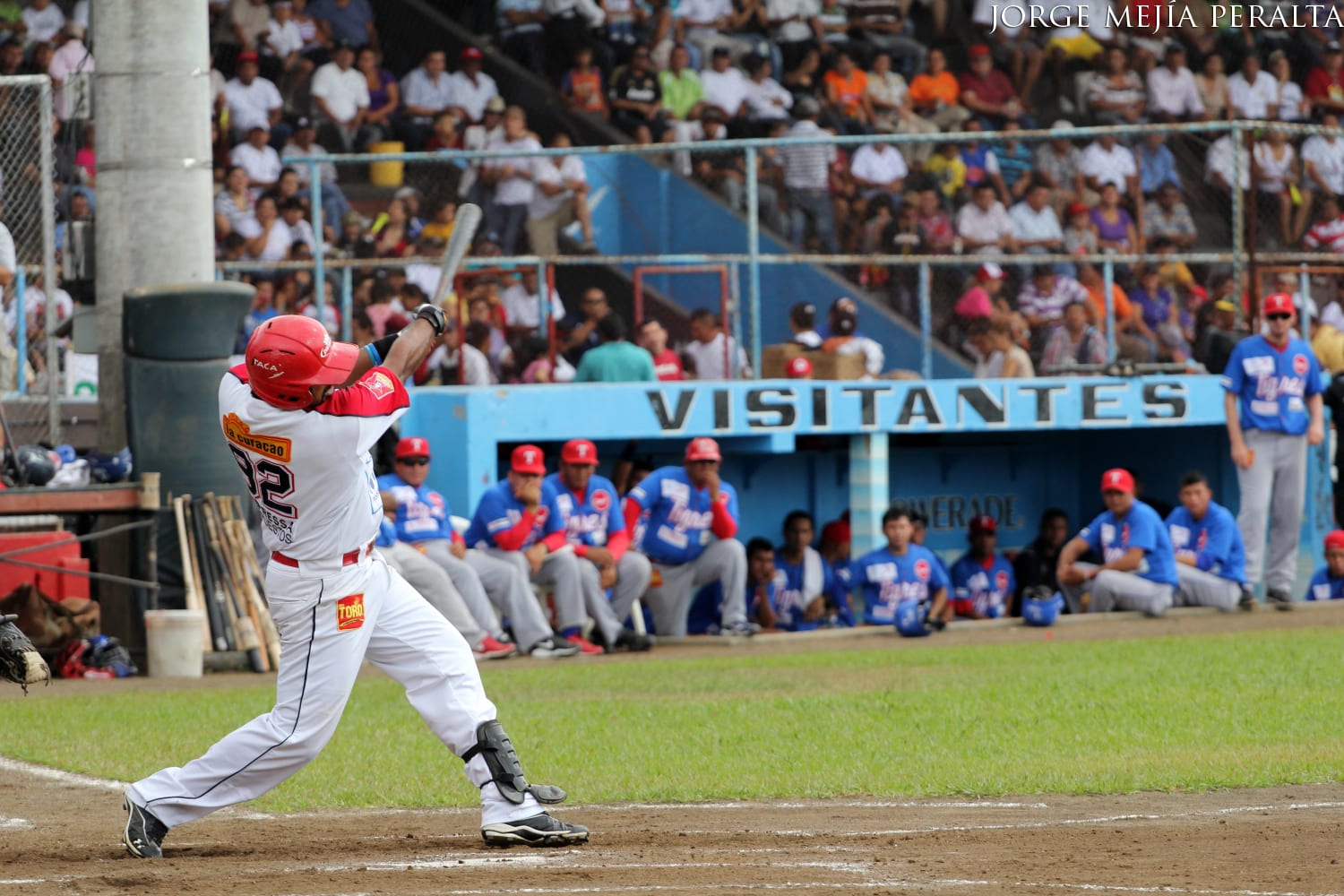 A baseball batter mid-swing at home plate in front of a packed, crowded stadium grandstand