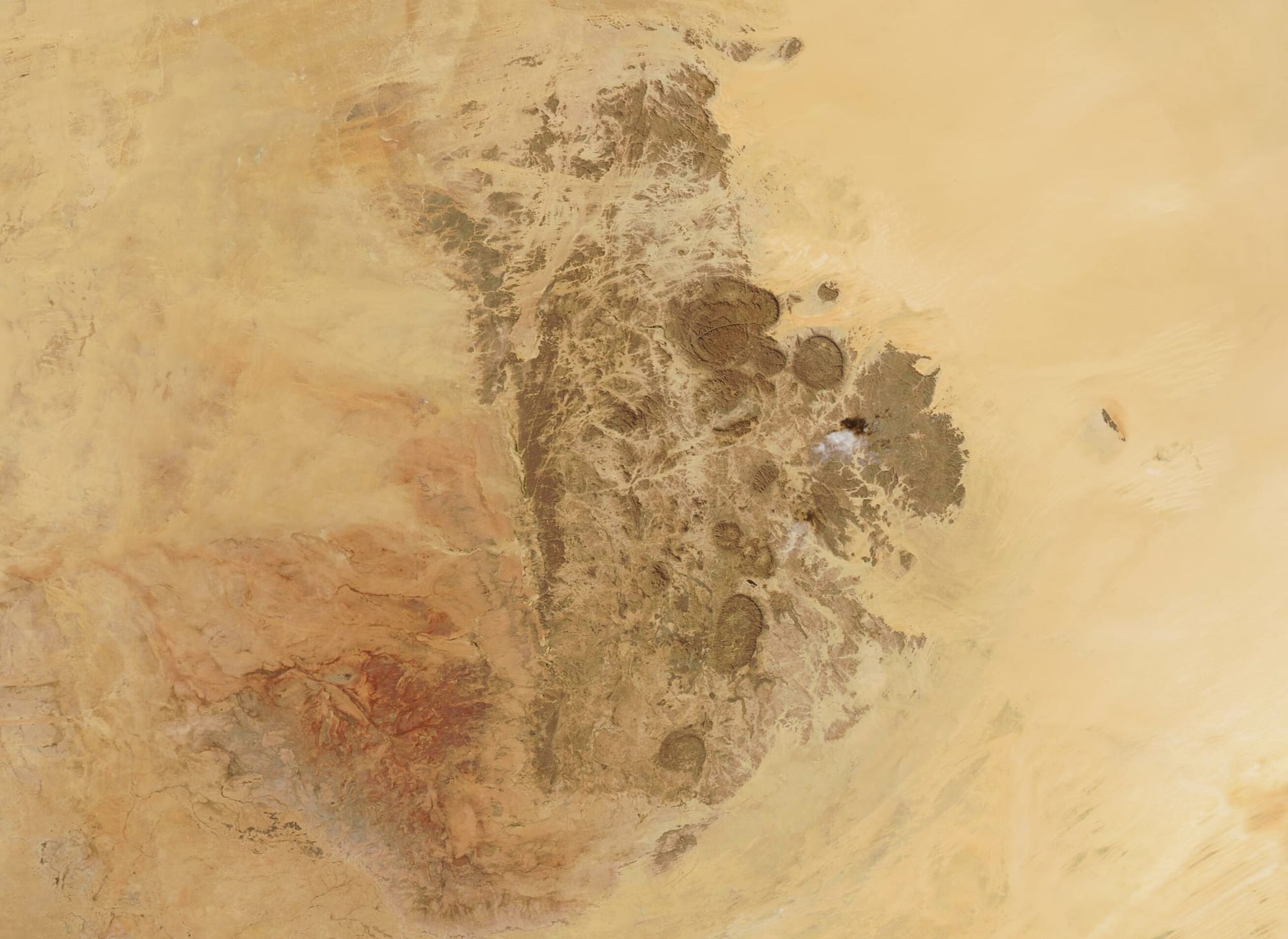 A rugged mountain range rising from a desert plain, seen from orbit