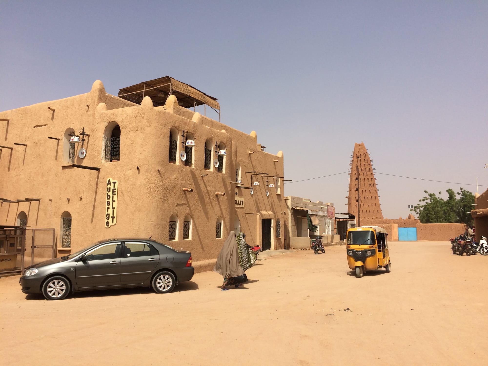 A tall mud-brick minaret with protruding wooden beams rising above a desert town