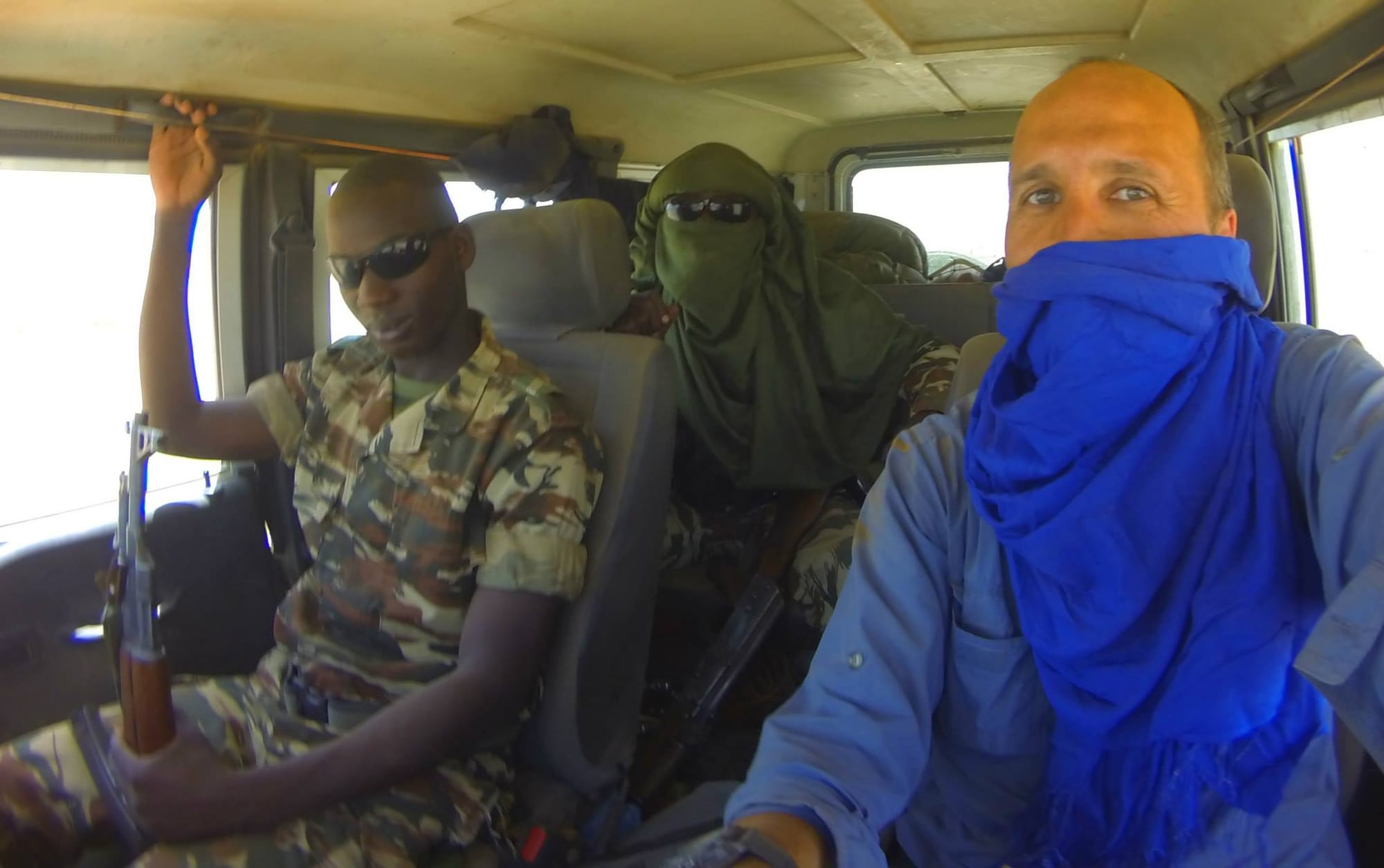 A vehicle and armed escort crossing an empty expanse of desert