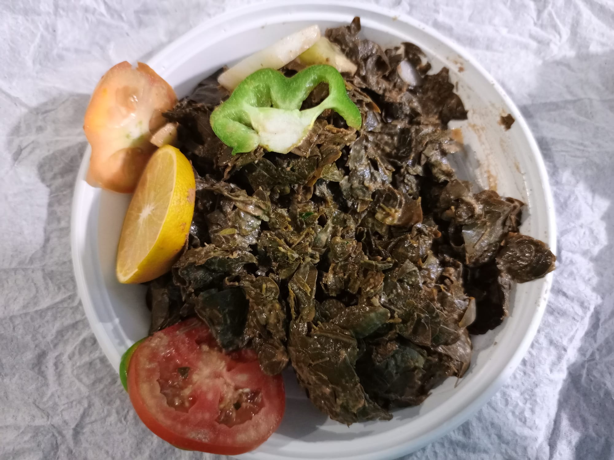 A plate of cooked moringa leaf sauce with tomato, pepper and lemon
