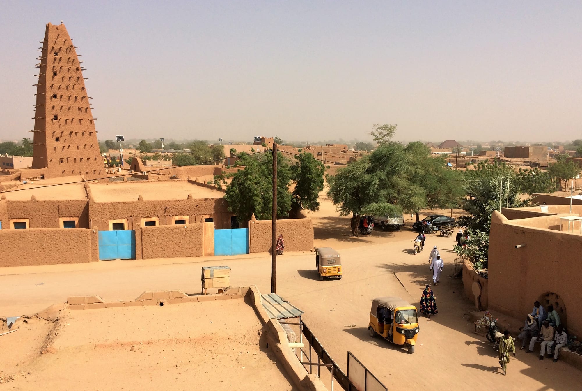 A tall mud-brick minaret bristling with wooden support beams, rising above the flat earthen roofs of Agadez