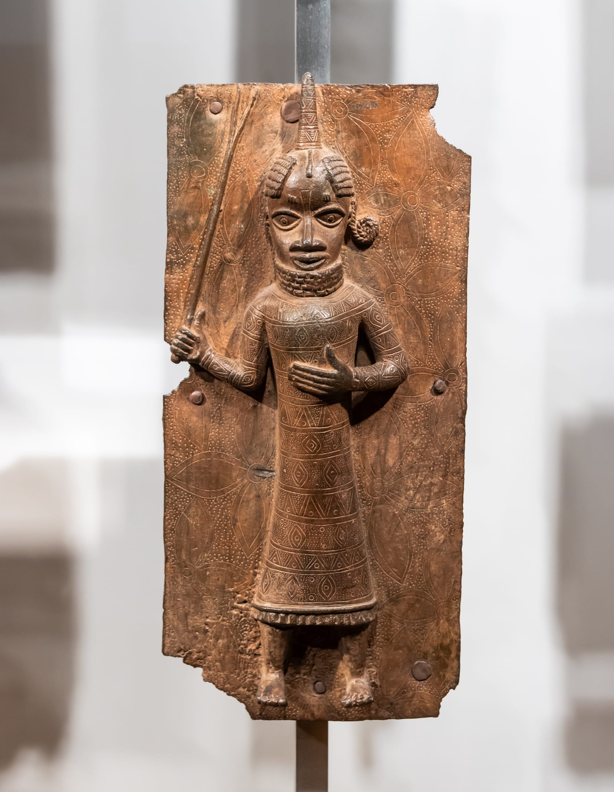Rows of ornate cast-brass relief plaques from Benin displayed in a museum case