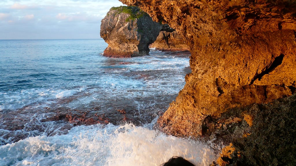 A large natural limestone arch on a rugged coastline with the sea visible through it