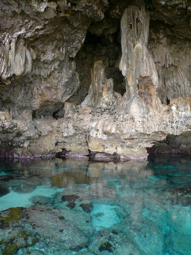 A large coastal limestone cave with a pool of clear water inside