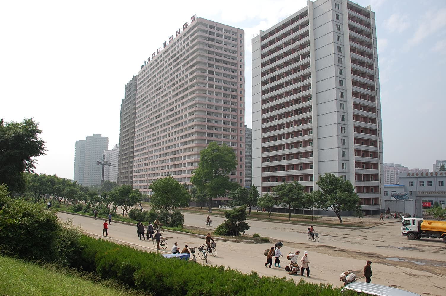 Rows of high-rise apartment blocks in Pyongyang with pedestrians, cyclists and a truck on the road in front