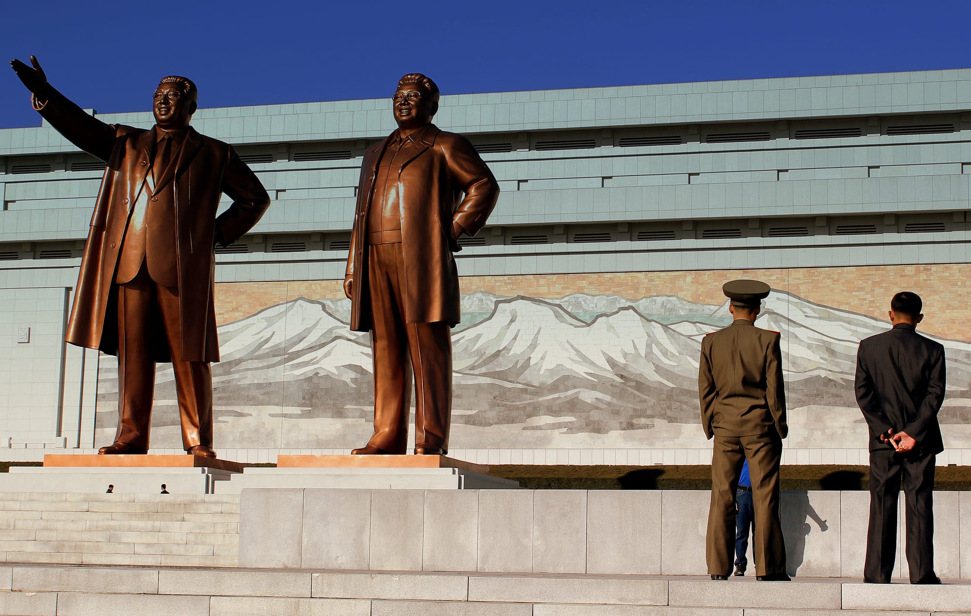 Two huge bronze statues of men in coats standing on a stepped plaza