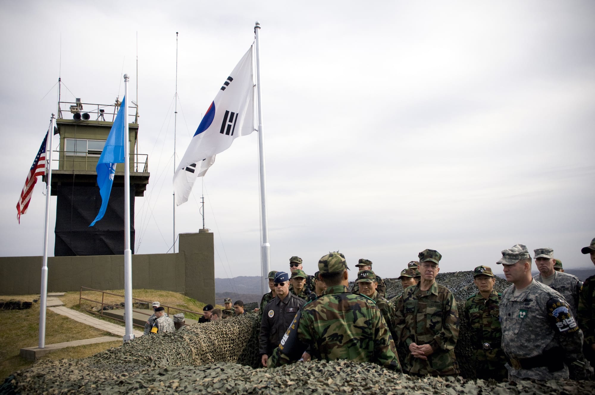 A group of officials standing at a demarcation line between two countries, with a guard post visible