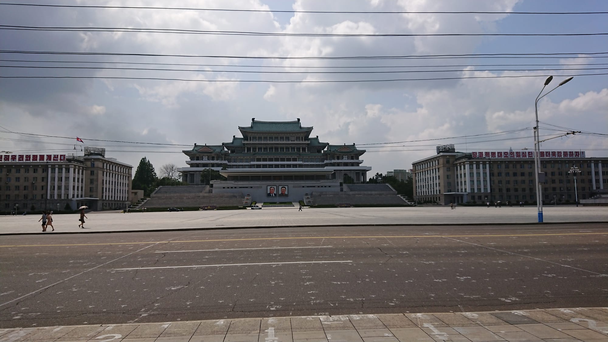 A vast paved plaza flanked by grand grey government buildings, with a portrait on the far facade