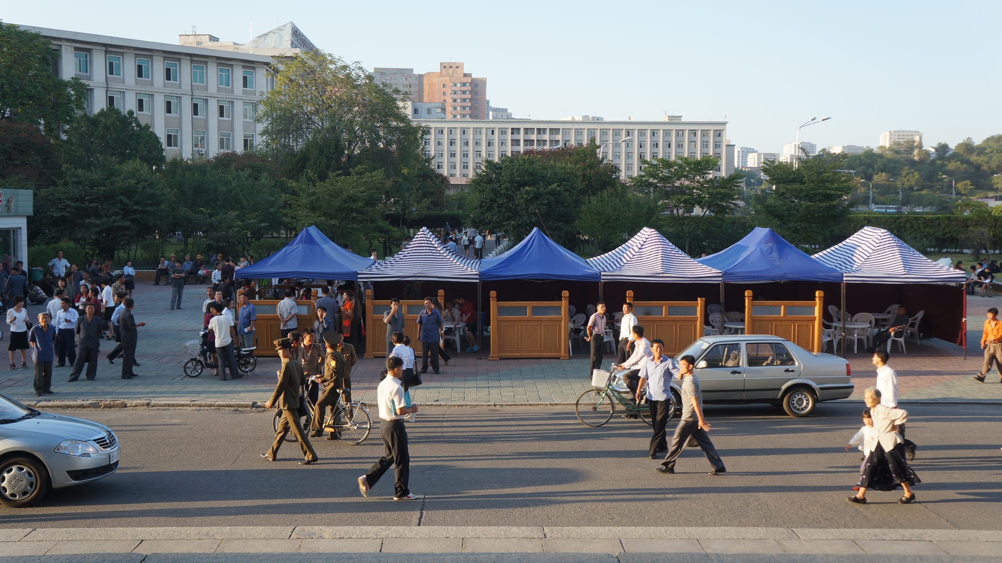 A row of street food vendor tents on a Pyongyang street with people passing by